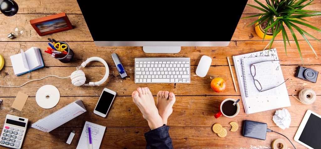 Businessman working in his office with feet on desk. Smart phone, tablet and various office supplies around the workplace. Flat lay.
